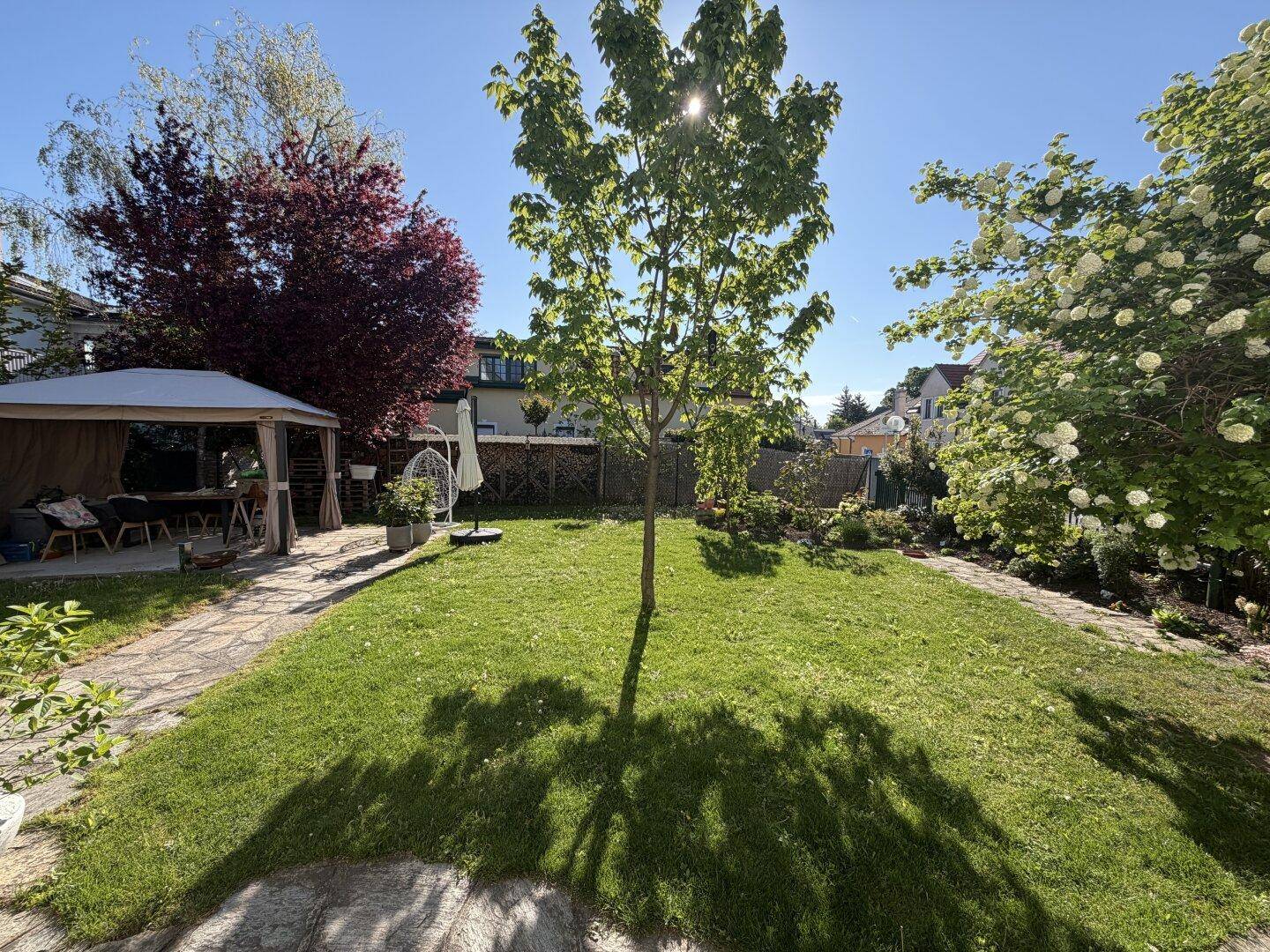 Gepflegter Garten mit großem Rasenbereich, einem Baum in der Mitte und einem Steinplattenweg.