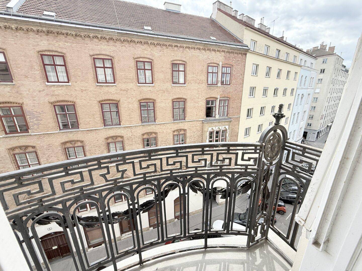 Blick von einem Balkon mit schmiedeeisernem Geländer auf die belebte Stadtstraße.