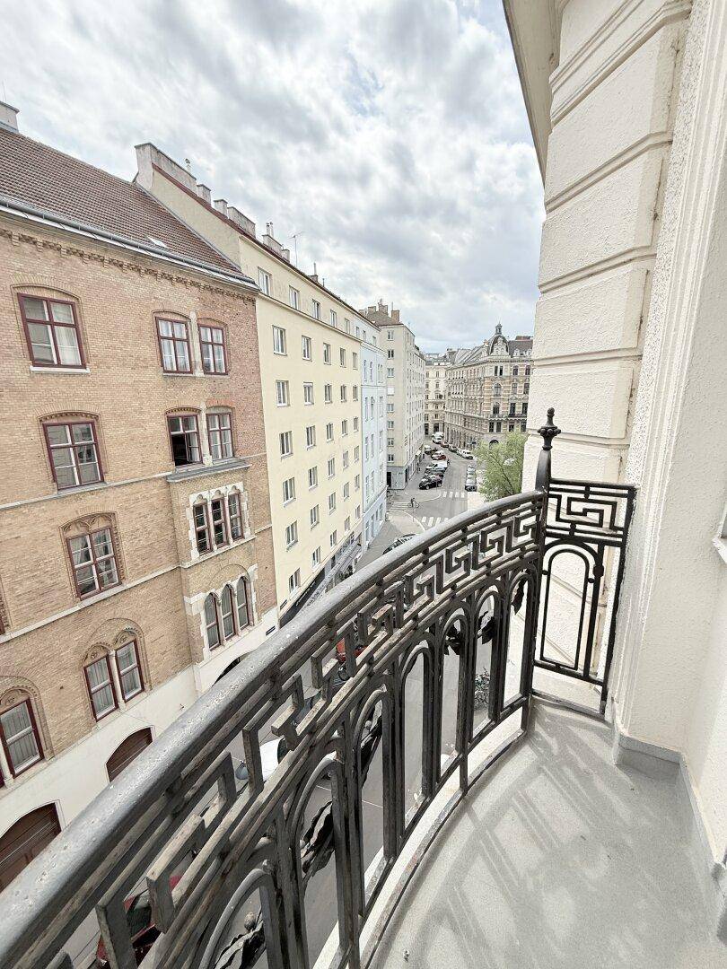 Blick von einem Balkon mit schmiedeeisernem Geländer auf die umliegenden Stadtgebäude und Straße.