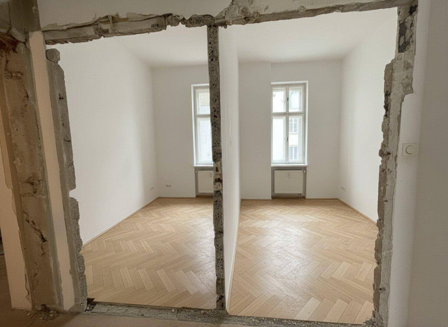 Zwei helle Räume mit Fischgrätparkett, getrennt durch eine teilweise entfernte Wand, in Renovierung.