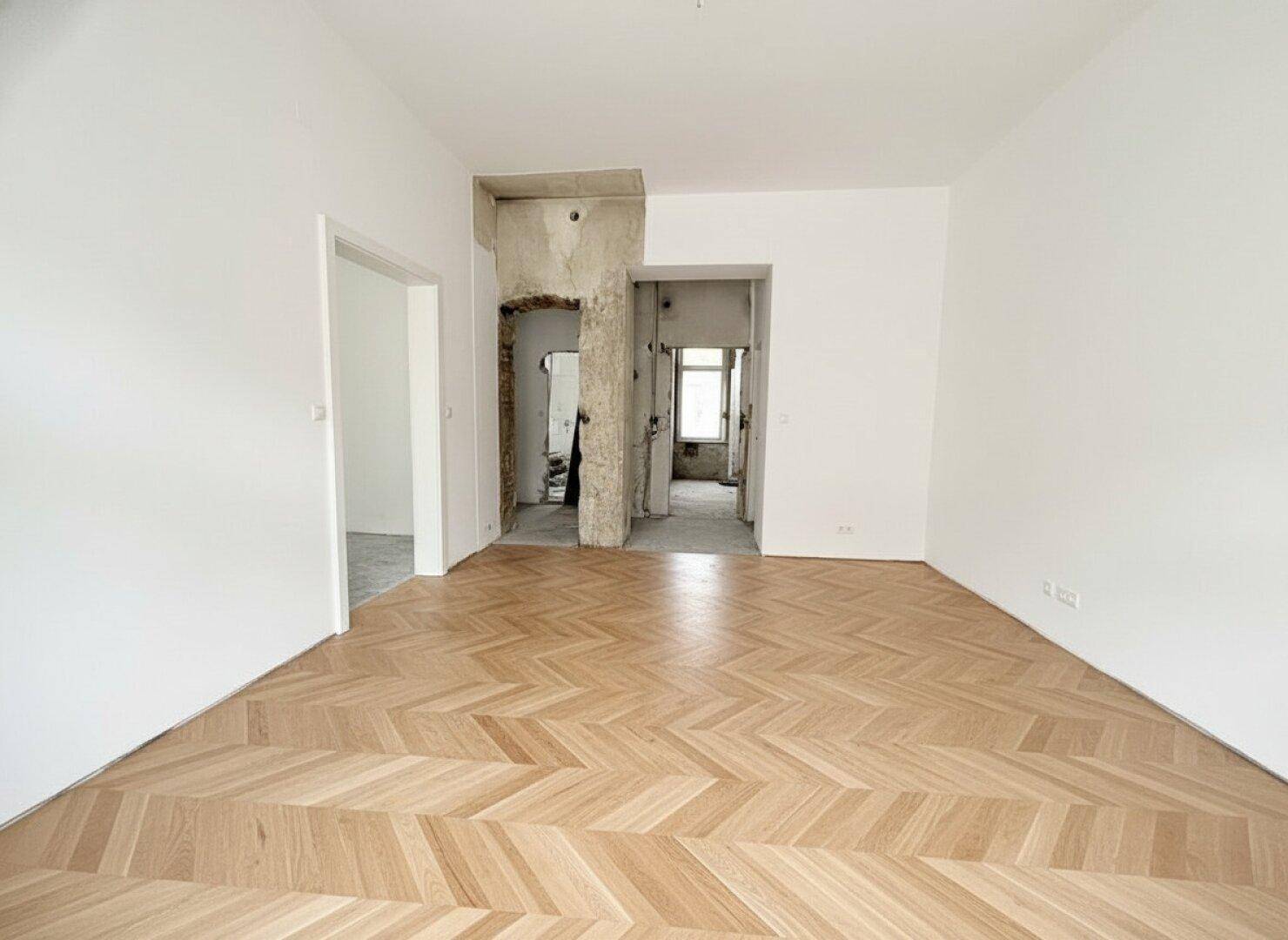 Geräumiger Raum mit Fischgrätparkett und sichtbaren Renovierungsarbeiten an den Wänden.