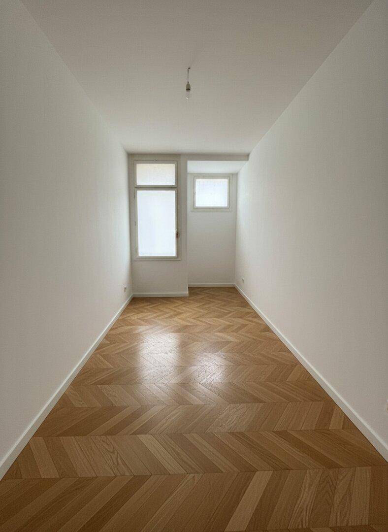 Schmaler, heller Raum mit Fischgrätparkett und zwei Fenstern, ideal für ein Büro oder Ankleidezimmer.