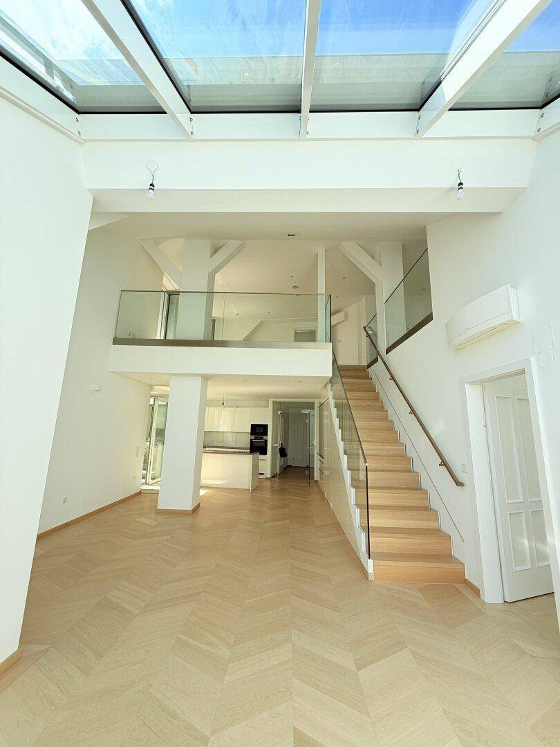 Offener Wohnbereich mit moderner Treppe, Glasgeländer und einem beeindruckenden Glasdach, das den Raum erhellt.