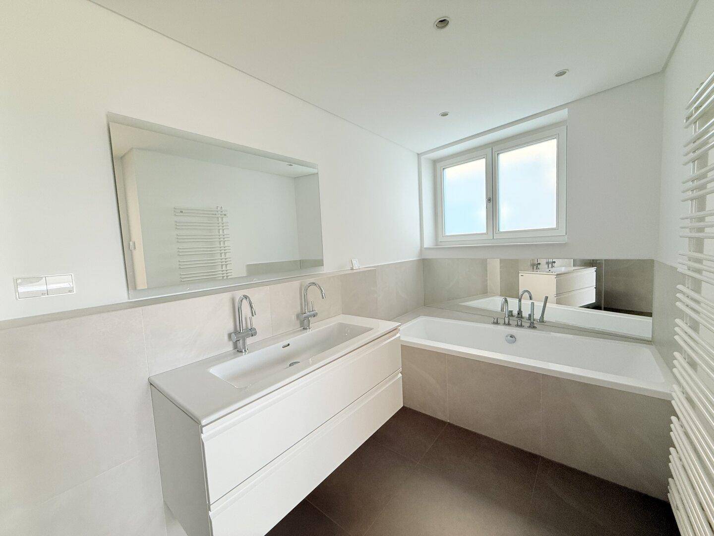 Helles Badezimmer mit moderner Badewanne, Einzelwaschbecken, großem Spiegel und Fenster für natürliches Licht.