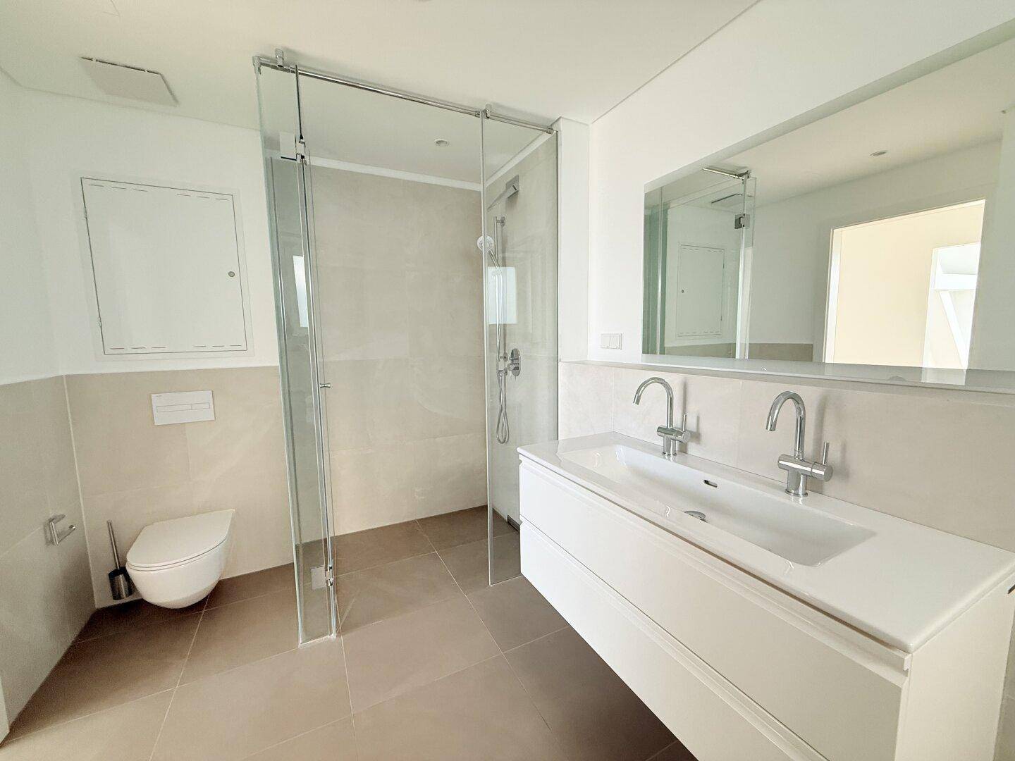 Modernes Badezimmer mit begehbarer Dusche, Einzelwaschbecken und wandhängendem WC in hellen Farbtönen.