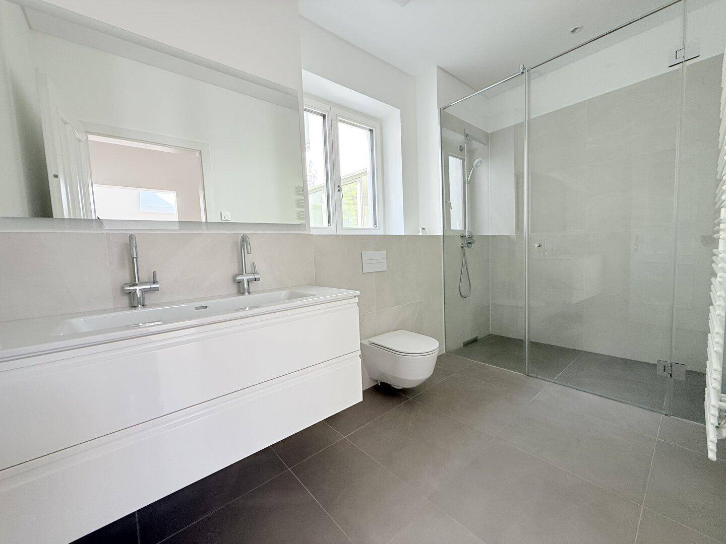 Modernes Badezimmer mit begehbarer Dusche, Einzelwaschbecken, wandhängendem WC und Fenster für Tageslicht.