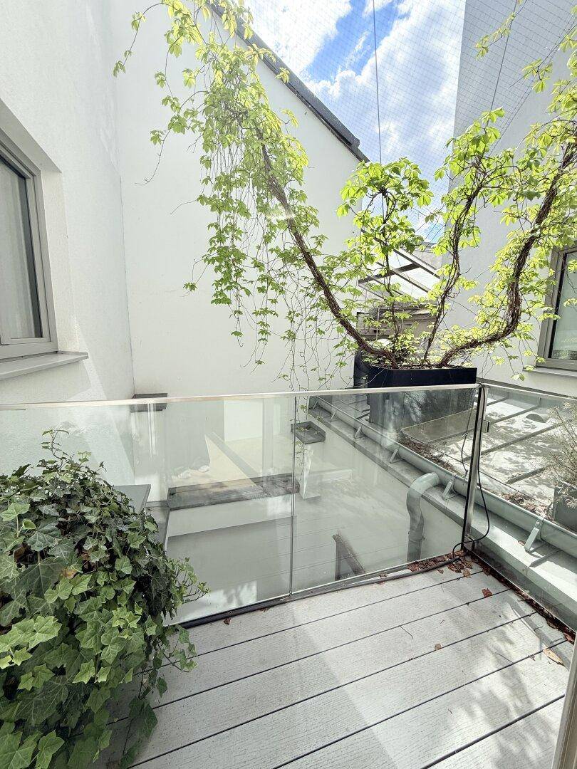 Sonnige Terrasse mit Holzdeck, Glasbrüstung und begrünten Wänden, ideal für entspannte Stunden im Freien.