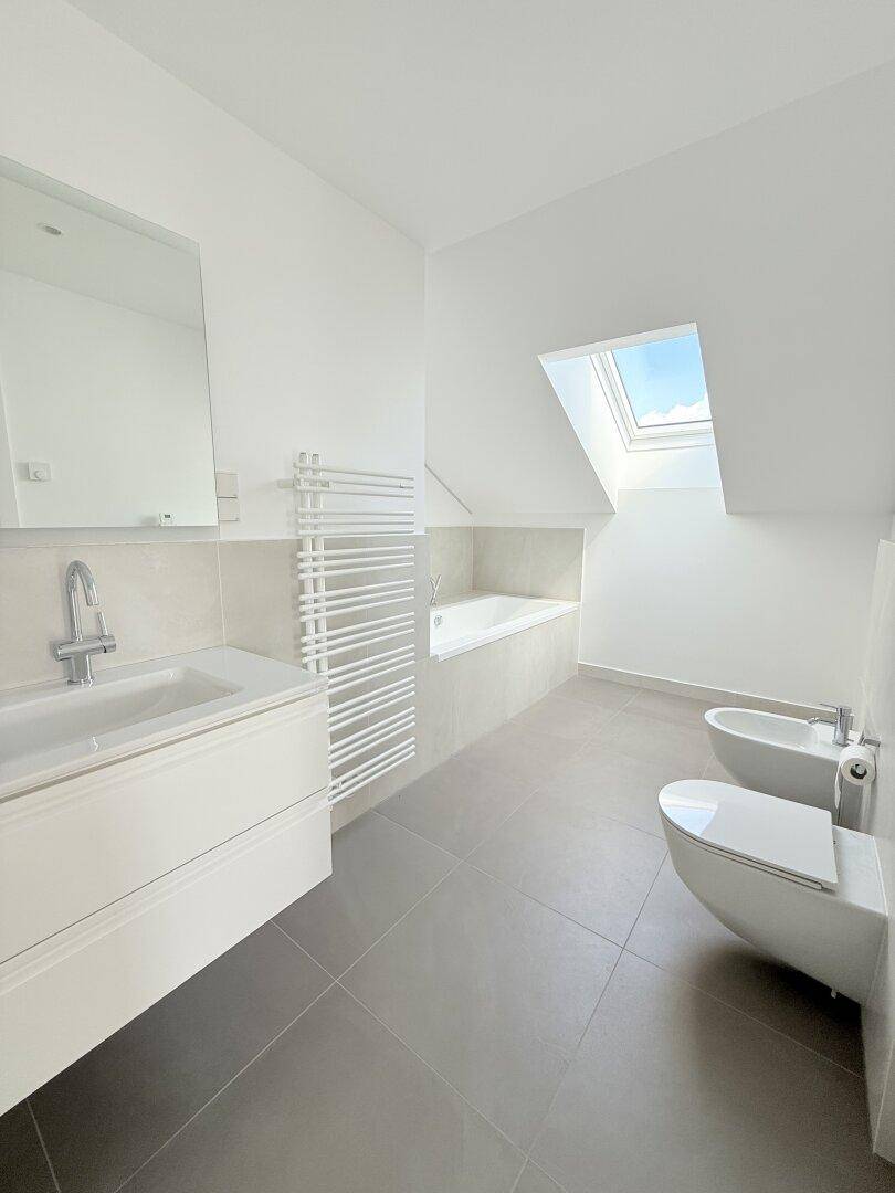 Modernes Badezimmer mit Badewanne, wandhängendem WC, Bidet und Dachfenster für eine helle Atmosphäre.
