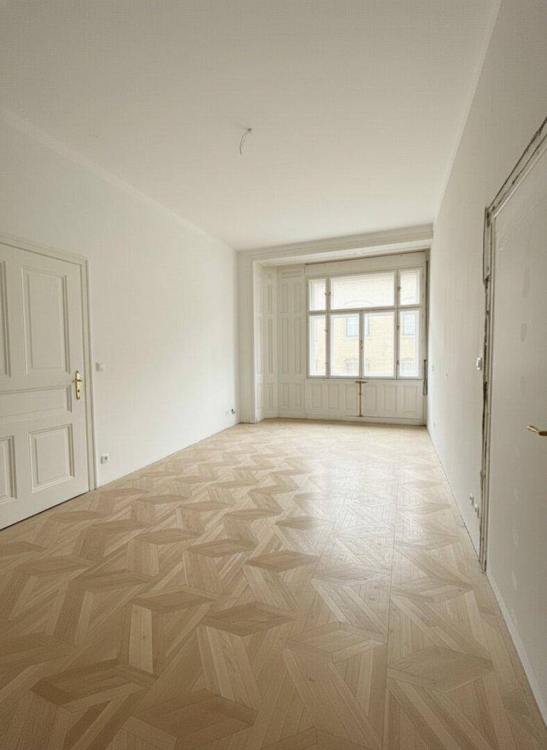 Leerer Raum mit elegantem Fischgrätparkett, hohen Decken und großen Fenstern.