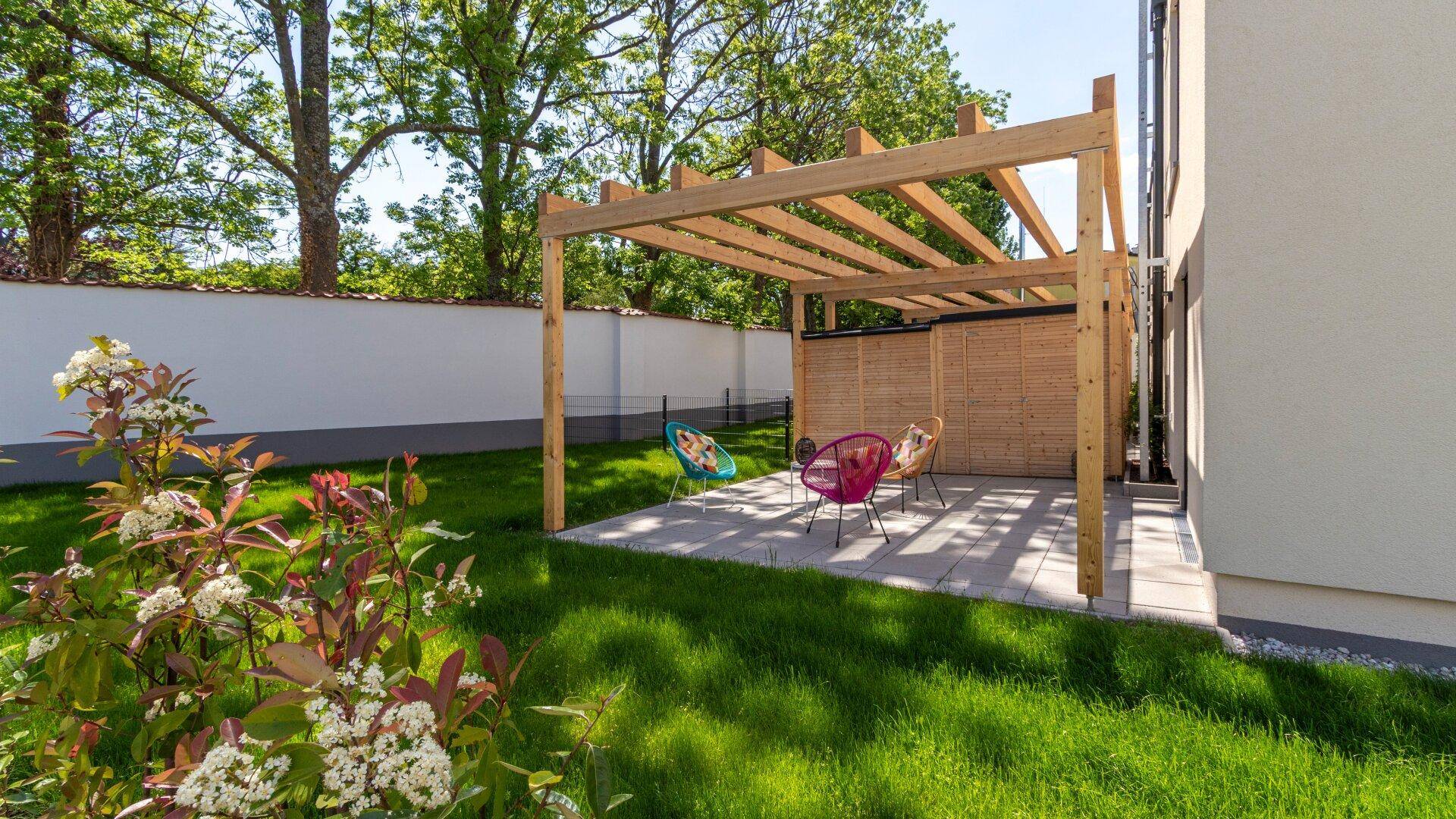 Gemütliche Terrasse mit Holzpergola und bunten Gartenmöbeln, umgeben von grünem Rasen.