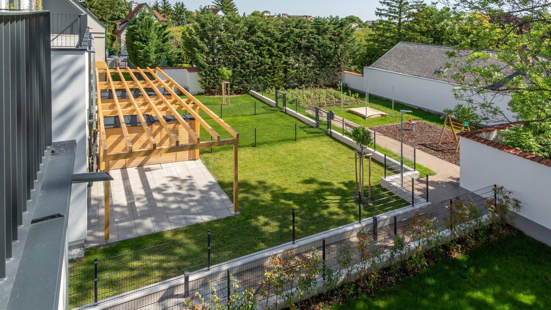 Vogelperspektive auf die Wohnanlage mit großem Garten, Spielplatz und privaten Terrassenbereichen.