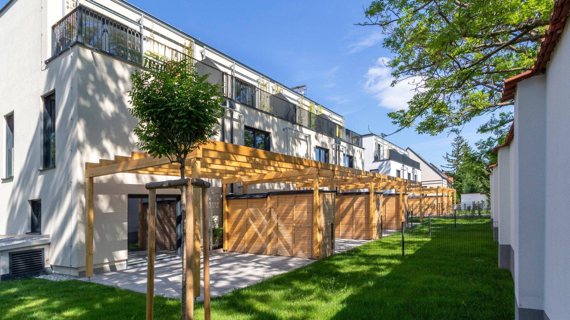 Moderne Reihenhäuser mit privaten Terrassen, Holzpergolen und gepflegten Grünflächen in sonniger Lage.