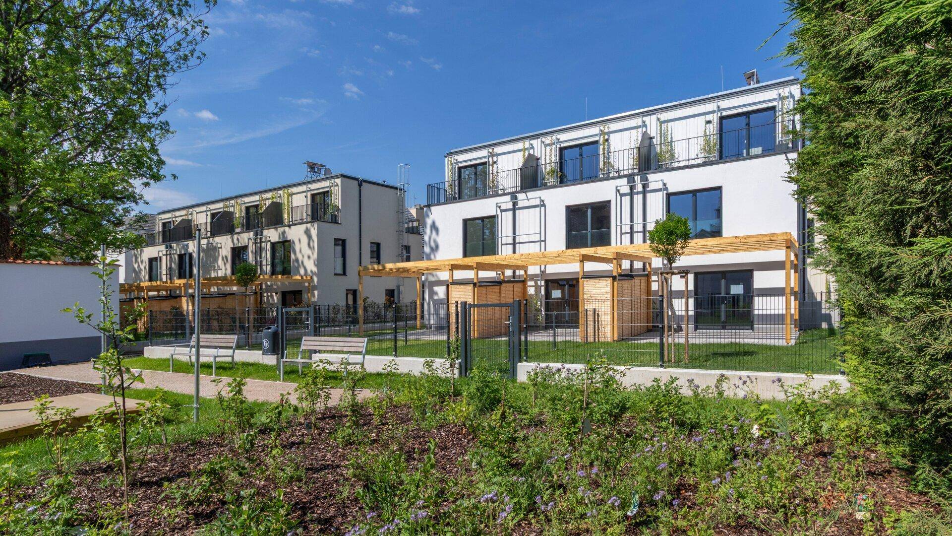 Moderne Wohngebäude umgeben einen Gemeinschaftsgarten mit Sitzbänken und Bepflanzung für Bewohner.