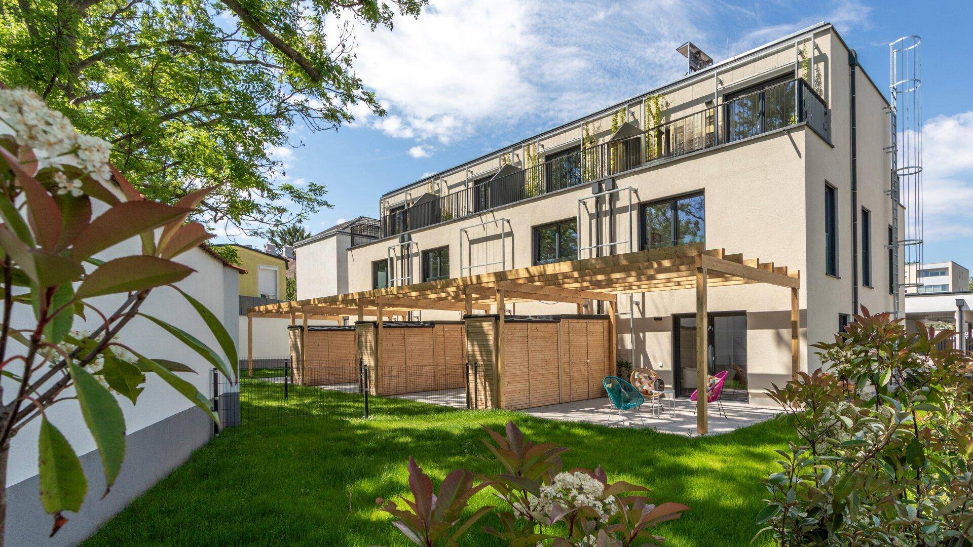 Seitenansicht der modernen Wohnanlage mit gepflegtem Garten und privaten Terrassenbereichen unter Holzpergolen.