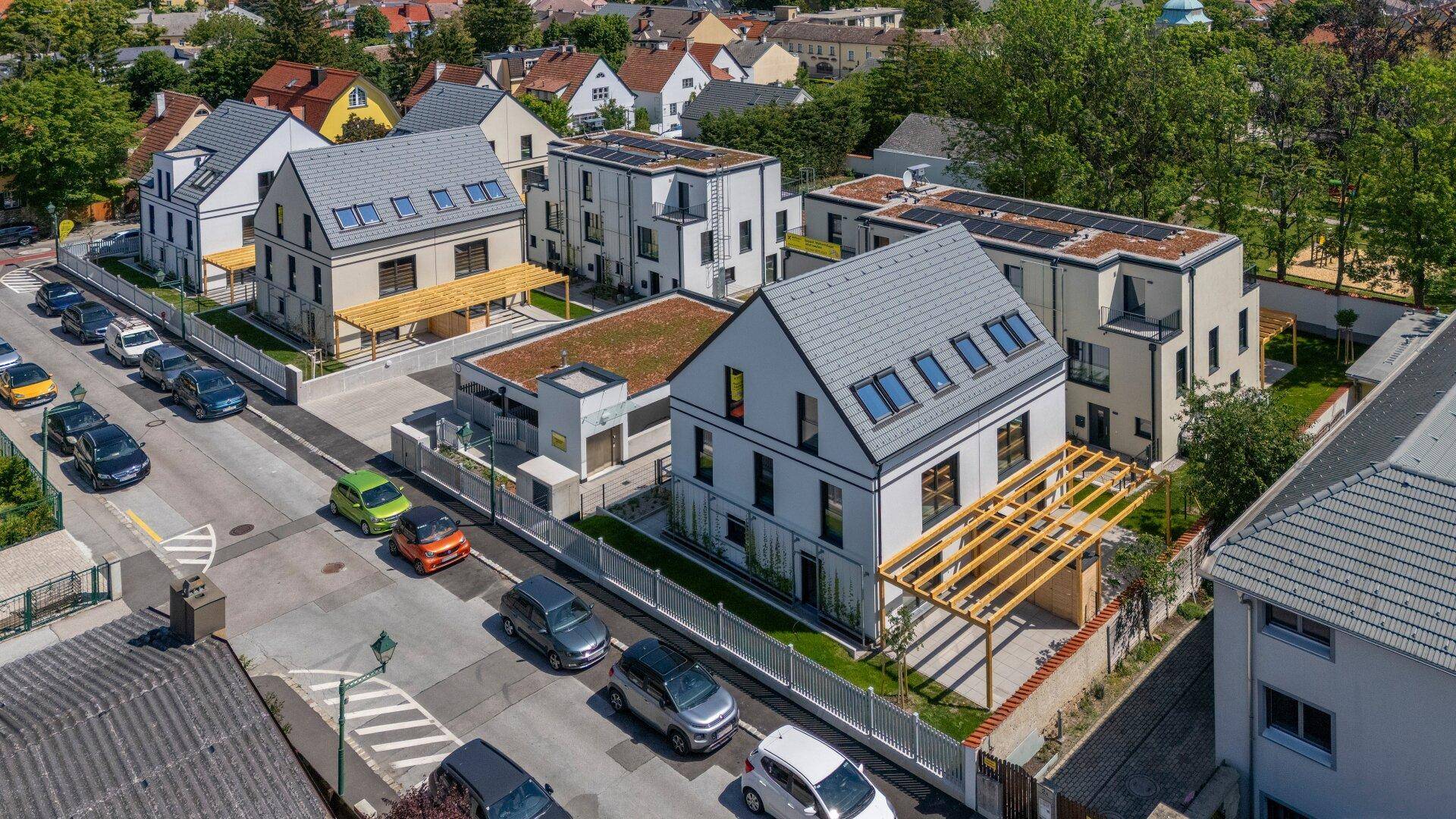 Luftaufnahme der modernen Wohnanlage mit mehreren Gebäuden, Gärten und Tiefgaragenzufahrt in der Nachbarschaft.