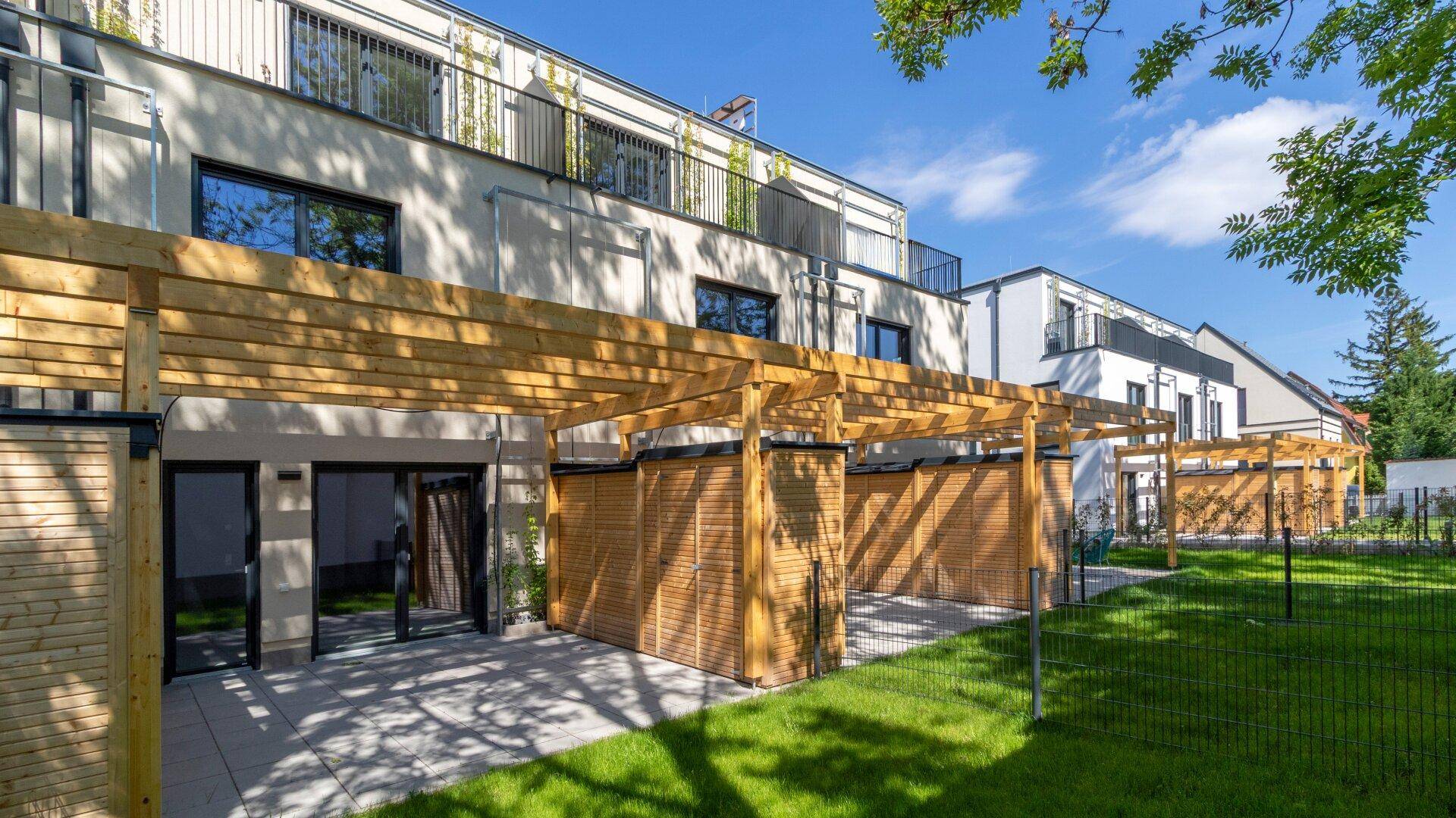Reihe moderner Wohngebäude mit Terrassen unter Holzpergolen und einer gemeinsamen Rasenfläche.