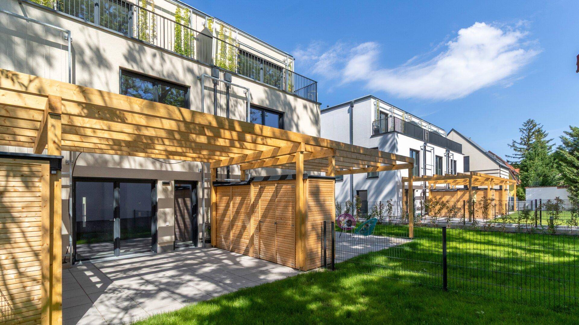 Moderne Wohngebäude mit Terrassen und Holzpergolen, umgeben von einem gepflegten Gemeinschaftsgarten.