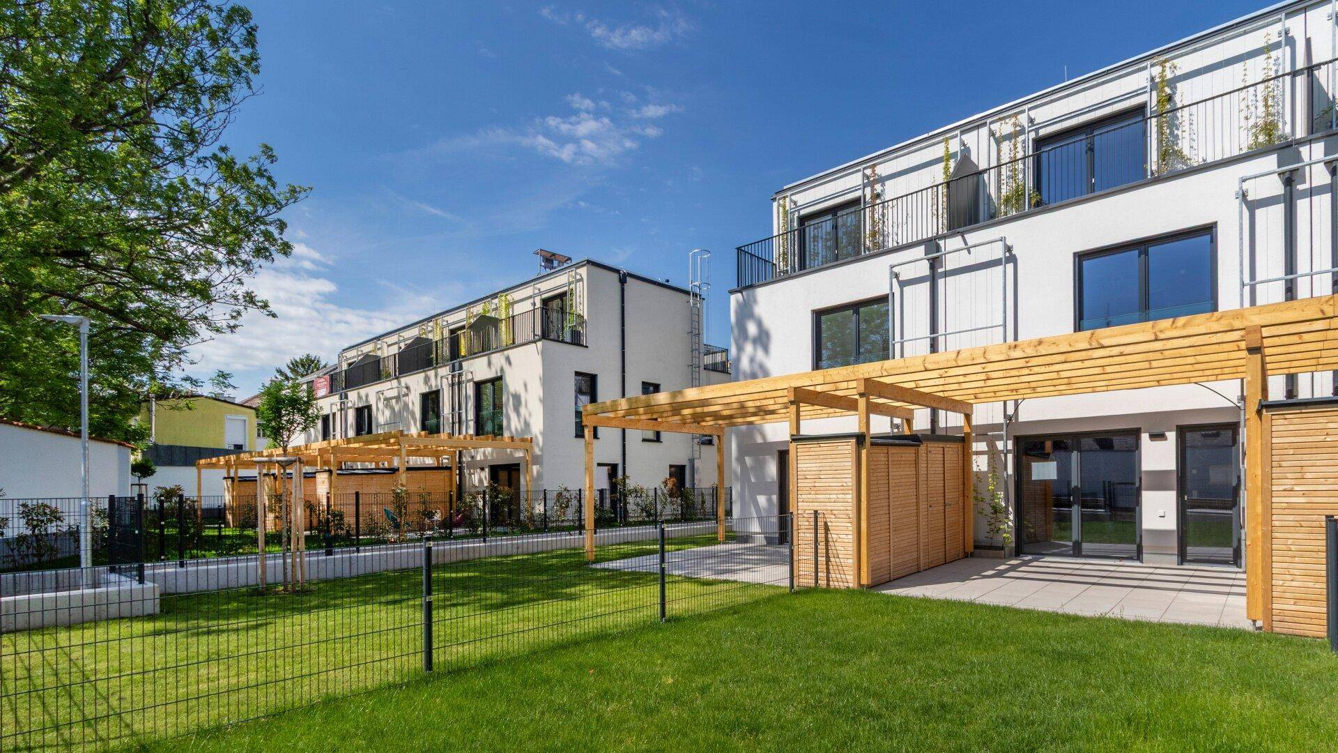 Moderne Wohngebäude mit Terrassen und Holzpergolen, angrenzend an eine weitläufige Rasenfläche.