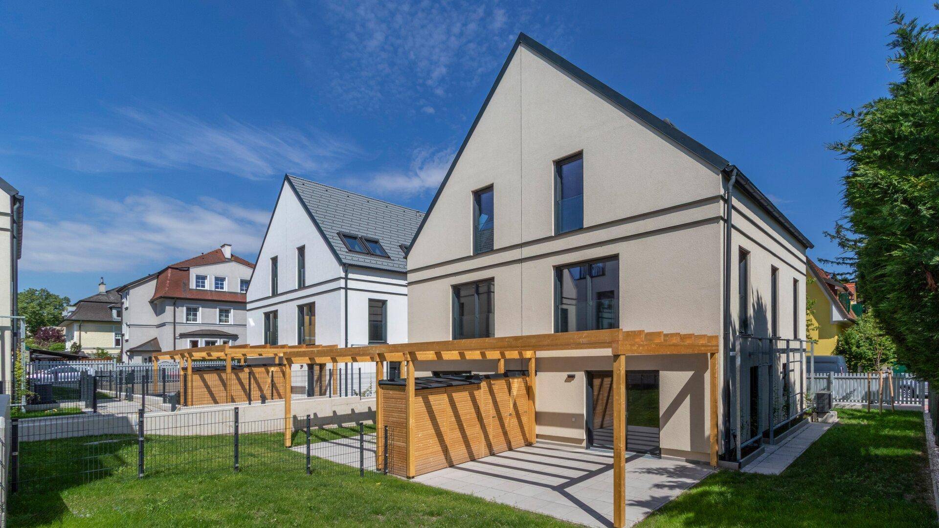 Zwei moderne Reihenhäuser mit Giebeldächern, hellen Fassaden und Holzpergolen in sonniger Lage.