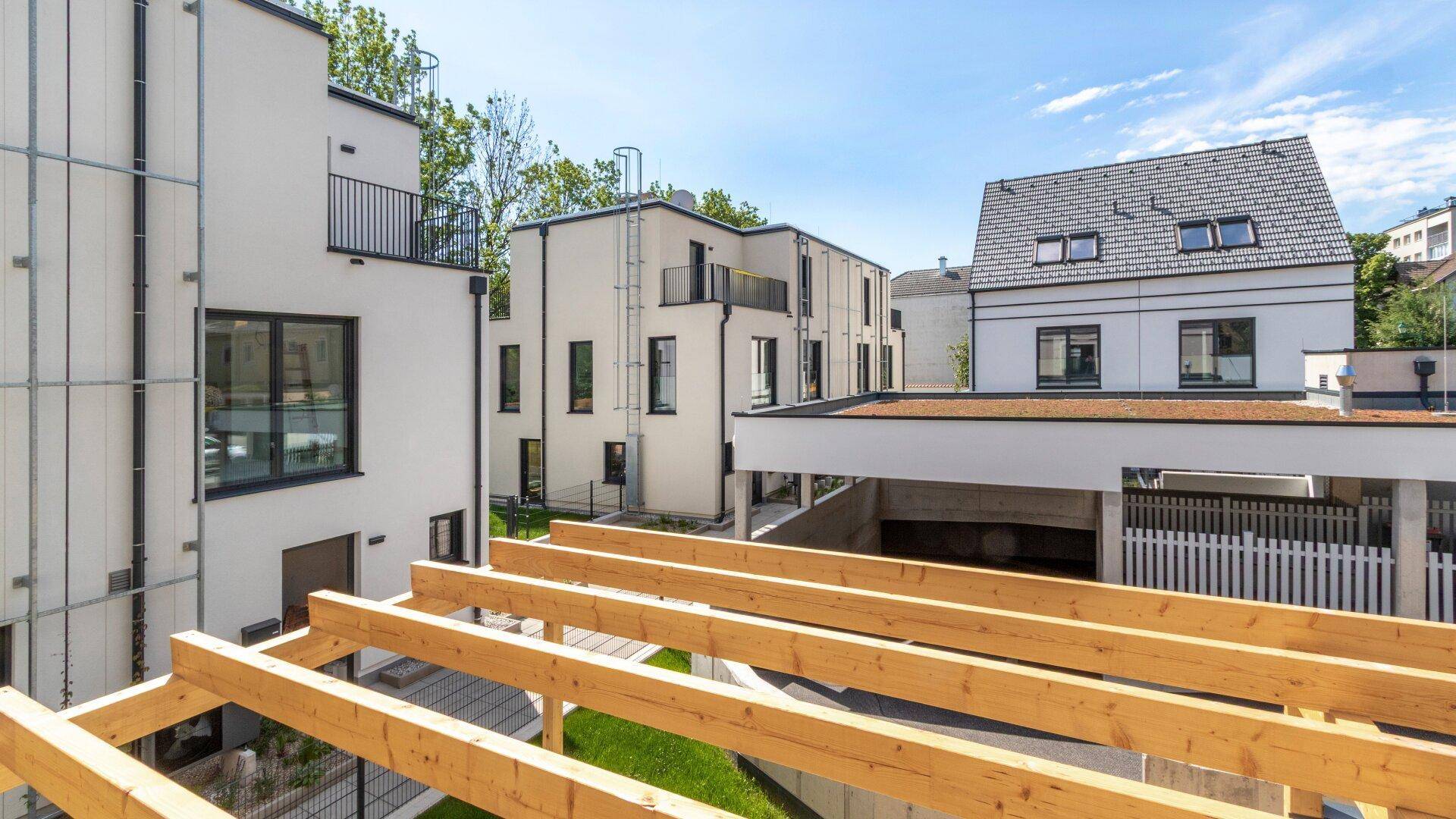 Blick auf moderne Wohngebäude mit Balkonen und einer Holzpergola im Vordergrund unter blauem Himmel.
