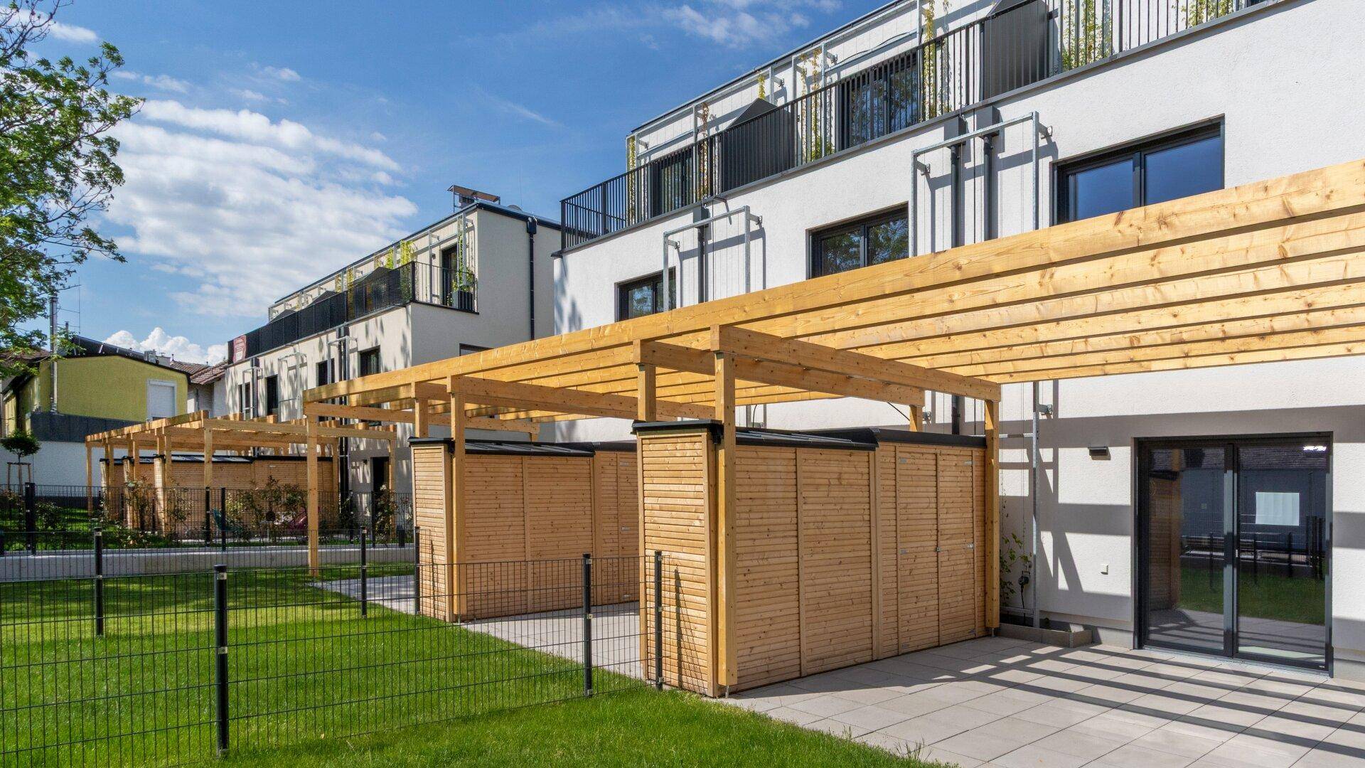 Reihe moderner Reihenhäuser mit Terrassen und Pergolen, umgeben von gepflegten Grünflächen.