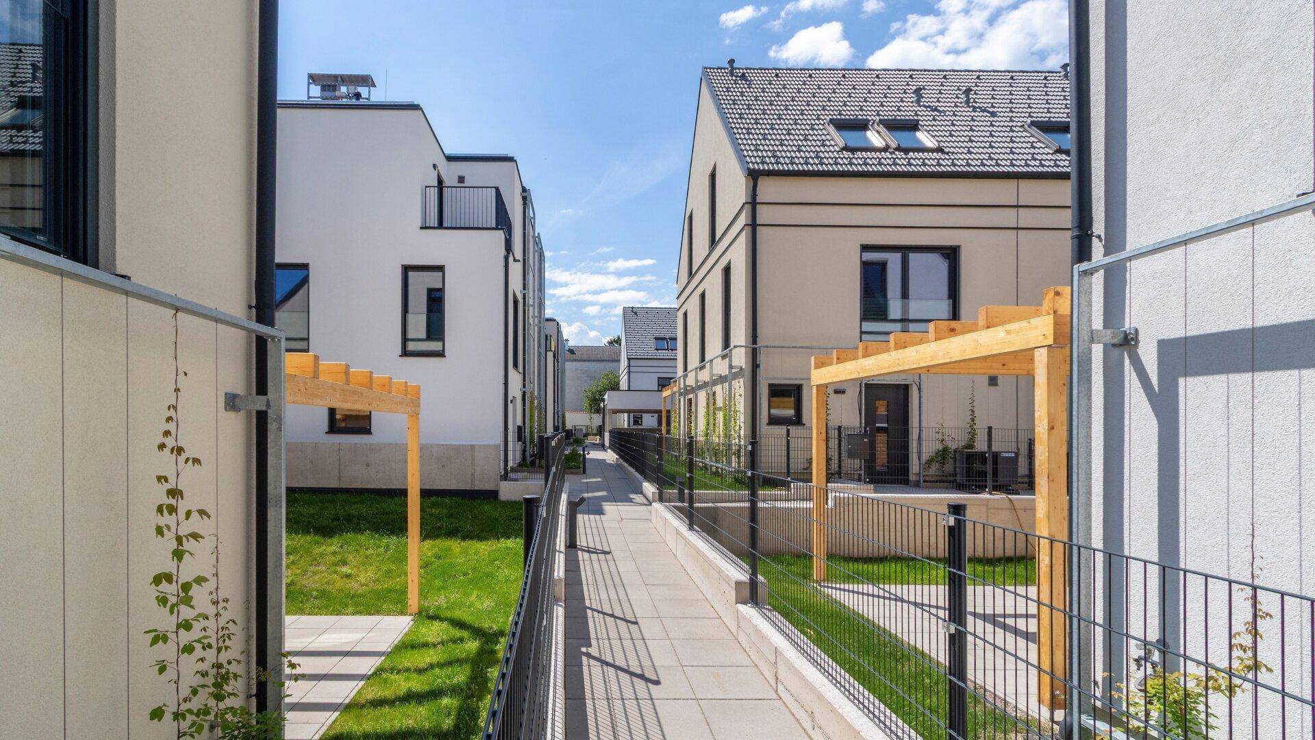 Seitlicher Zugangsweg zwischen modernen Reihenhäusern mit begrünten Wänden und gepflastertem Gehweg.