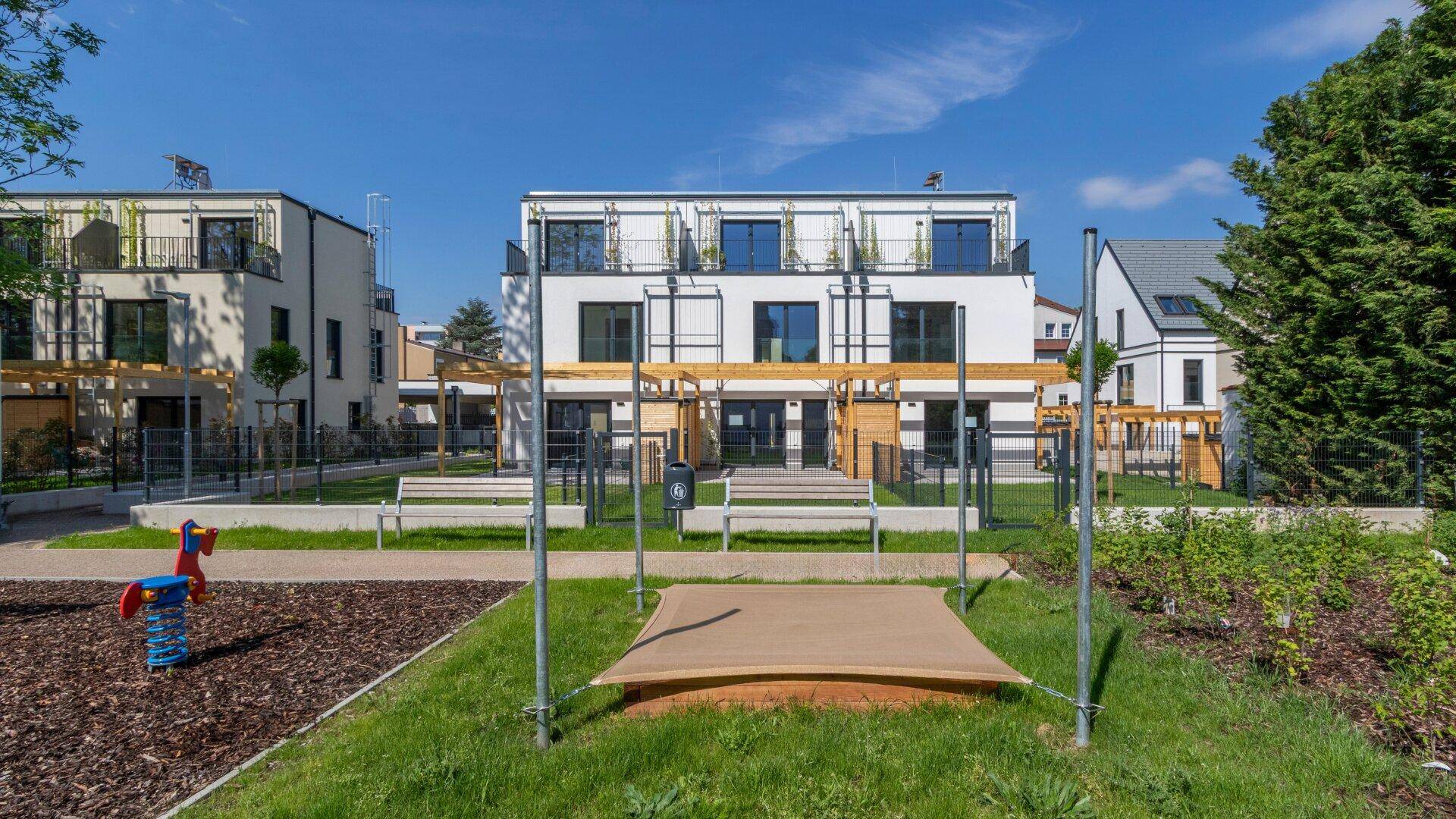 Moderne Wohnanlage mit einem Spielplatz, Sandkasten und Bänken im Gemeinschaftsgarten.