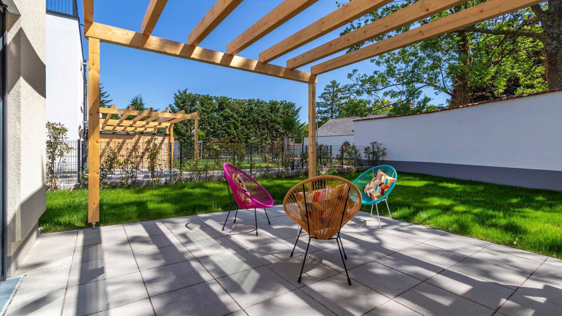 Sonnige Terrasse mit moderner Pergola, bunten Sitzgelegenheiten und Zugang zum Garten.