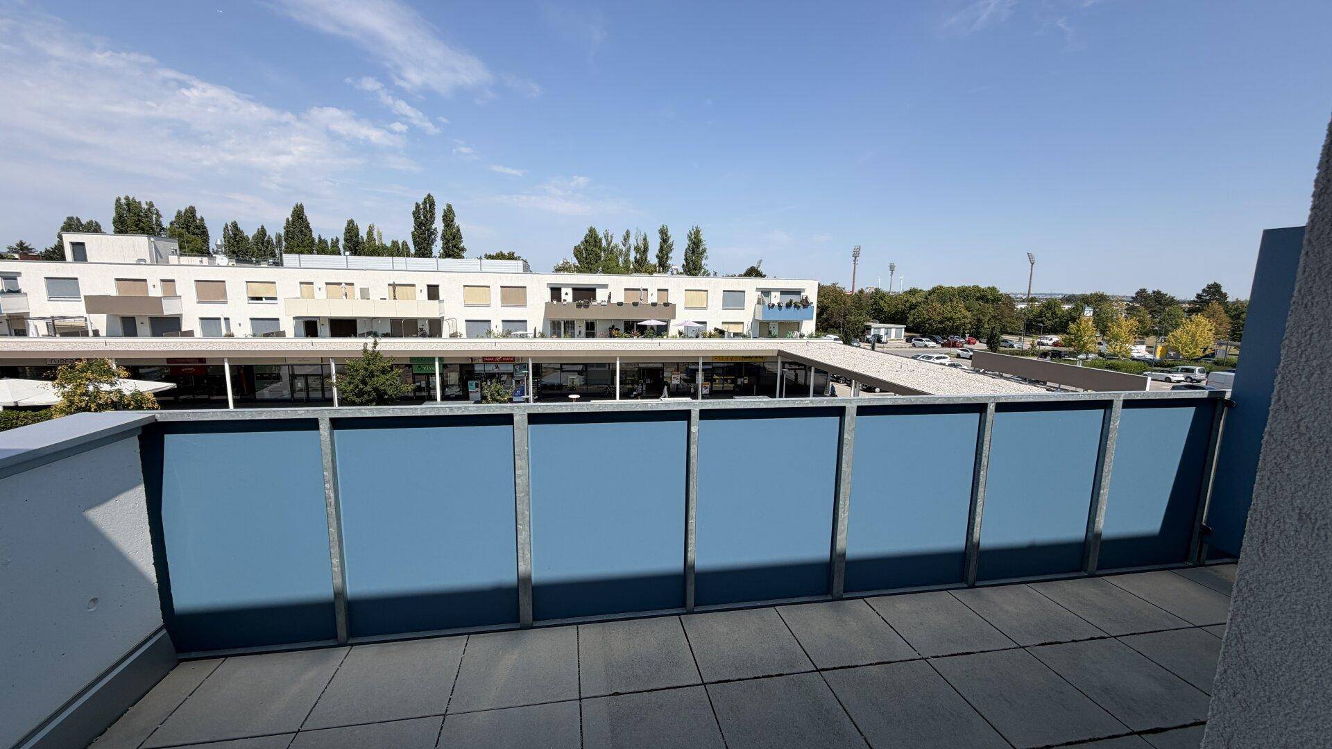 Geräumige Terrasse mit blauer Brüstung und weitem Blick auf die umliegenden Gebäude und Grünflächen.