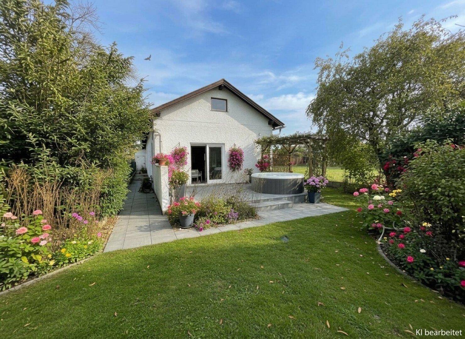 Gepflegter Garten mit Terrasse, Whirlpool und üppiger Blumenpracht hinter dem Haus.