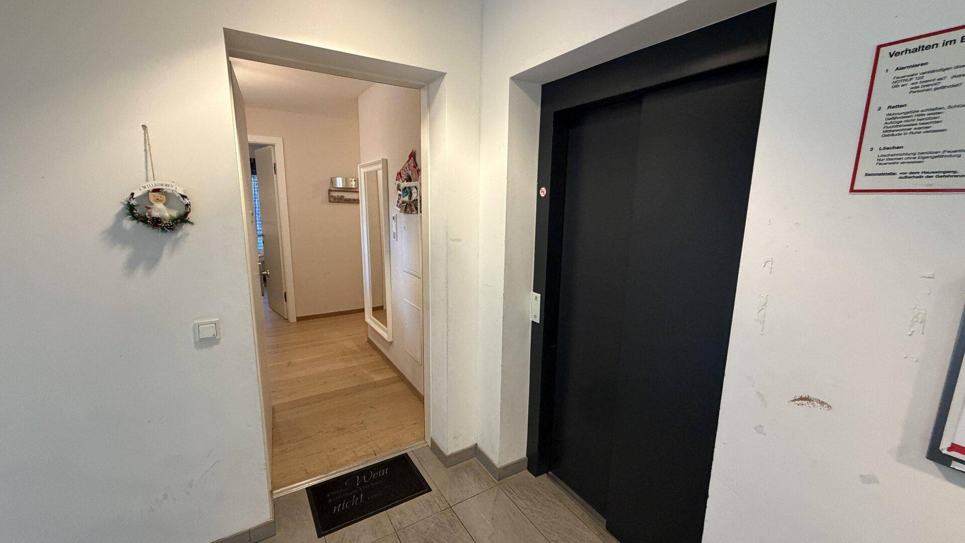 Flur mit Aufzug und Zugang zu einer Wohnung, gekennzeichnet durch eine schwarze Aufzugstür.
