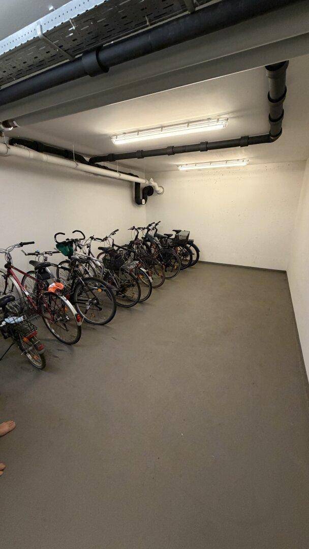 Fahrradraum im Untergeschoss mit zahlreichen abgestellten Fahrrädern und sichtbaren Leitungen an der Decke.