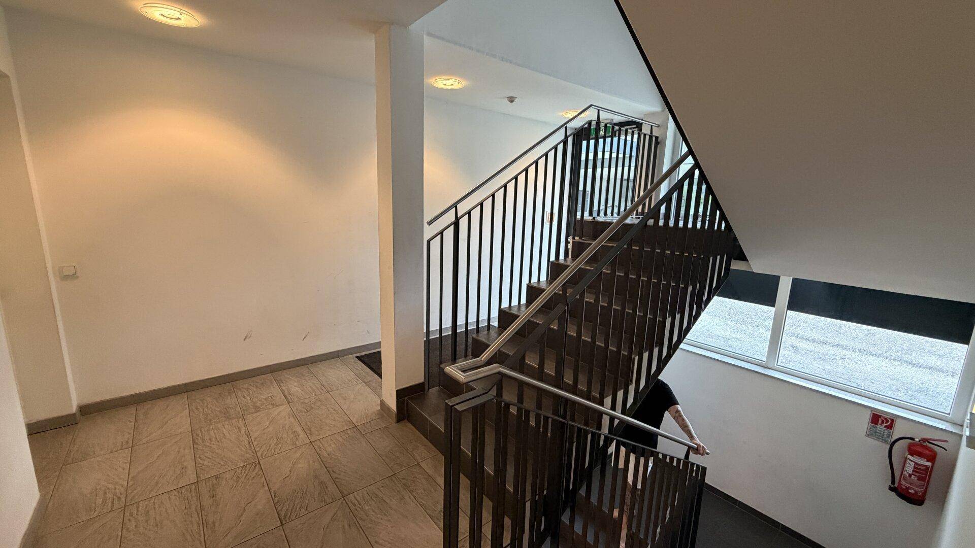 Modernes Treppenhaus mit Metallgeländer und Fliesenboden in einem Mehrfamilienhaus.