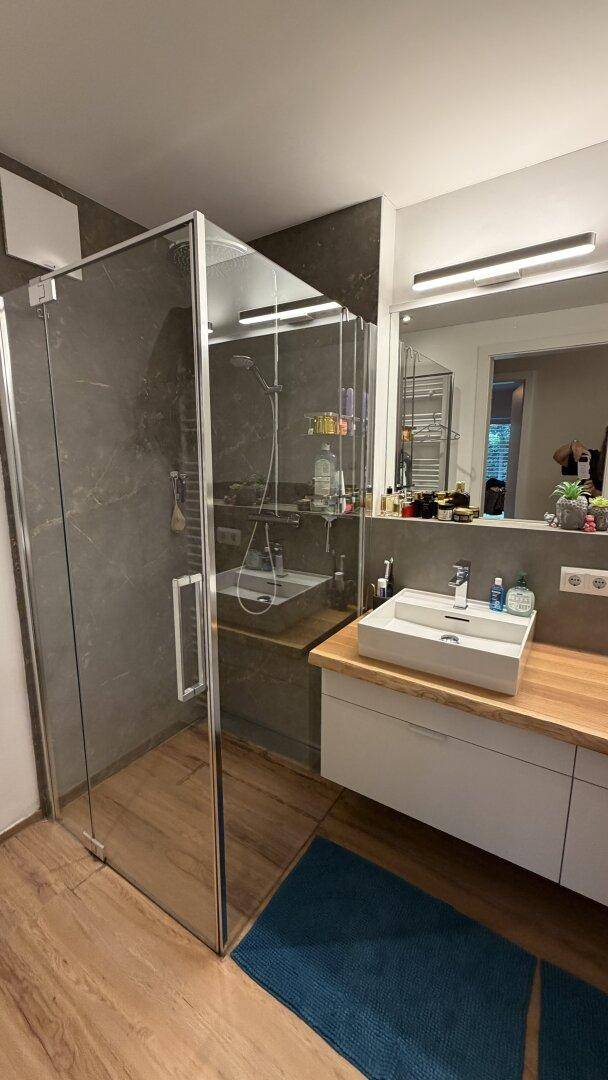 Modernes Badezimmer mit begehbarer Dusche, Holzarbeitsplatte und eleganten Fliesen.