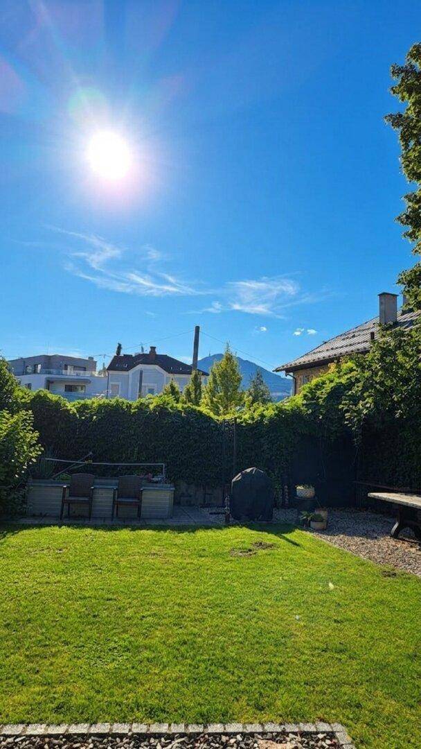 Sonniger Garten mit Rasenfläche, Sitzgelegenheiten und einem malerischen Bergblick im Hintergrund.