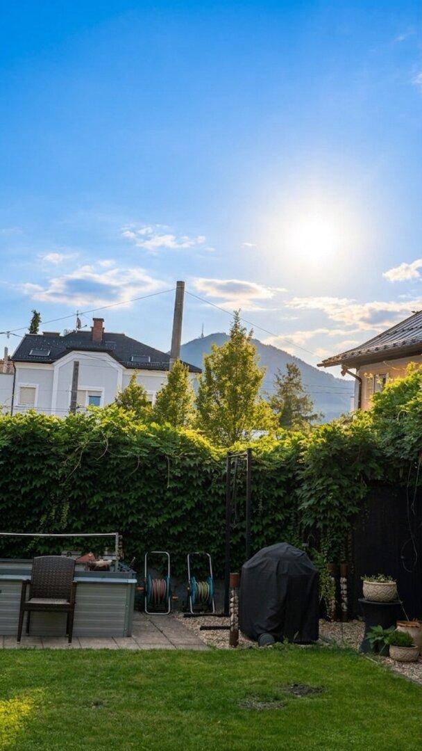 Gepflegter Garten mit Rasenfläche, hoher Hecke und einem malerischen Bergblick.