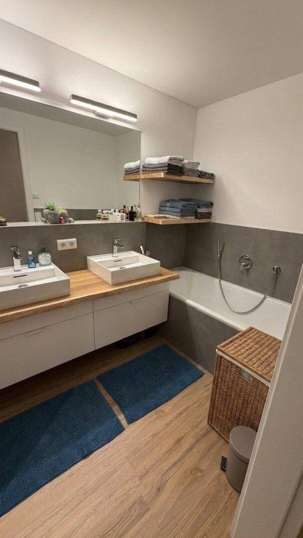 Helles Badezimmer mit zwei Waschbecken, Badewanne und modernen Holzdetails.