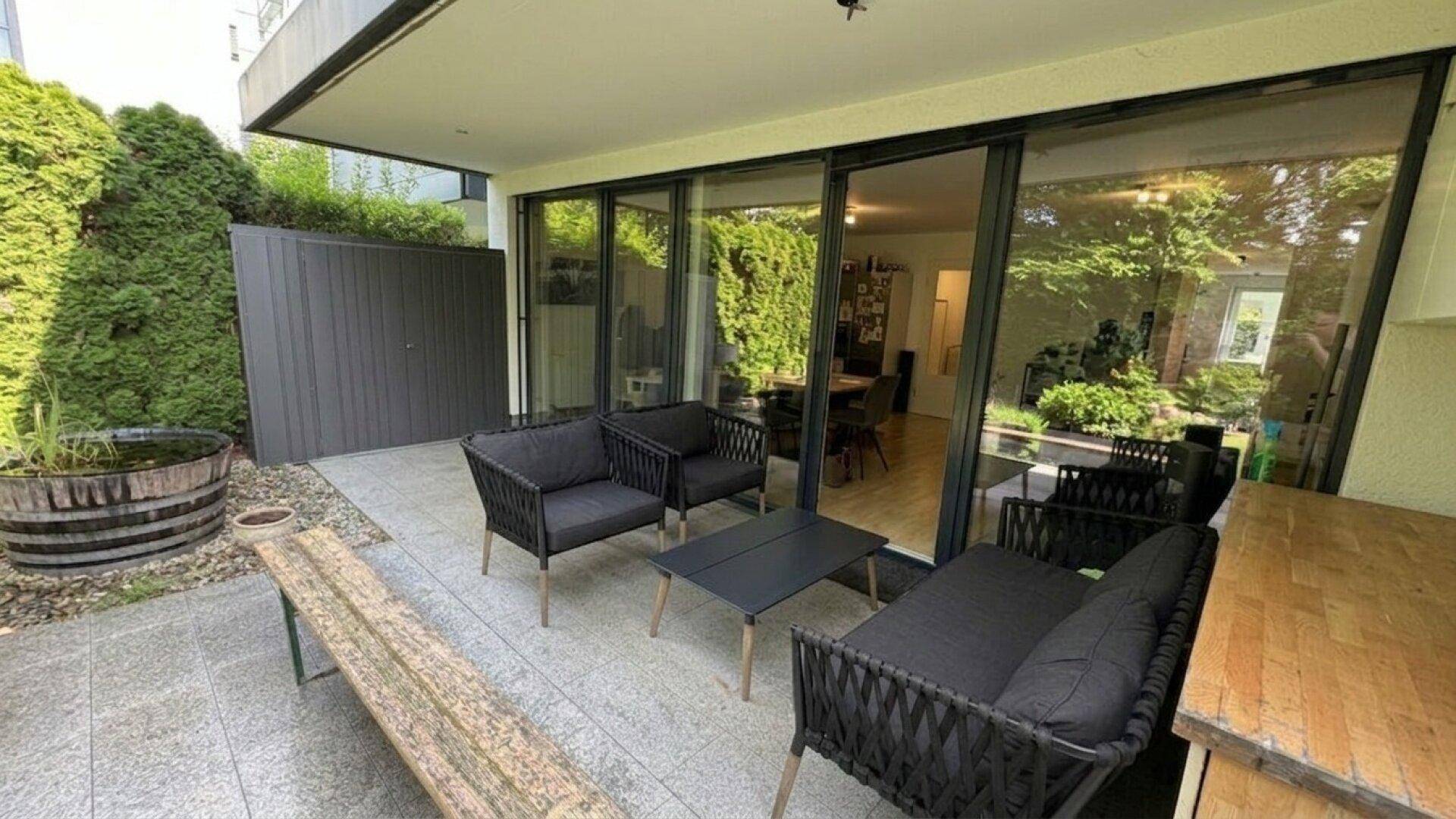 Gemütliche Terrasse mit modernen Outdoor-Möbeln und großen Glasschiebetüren zum Wohnbereich.