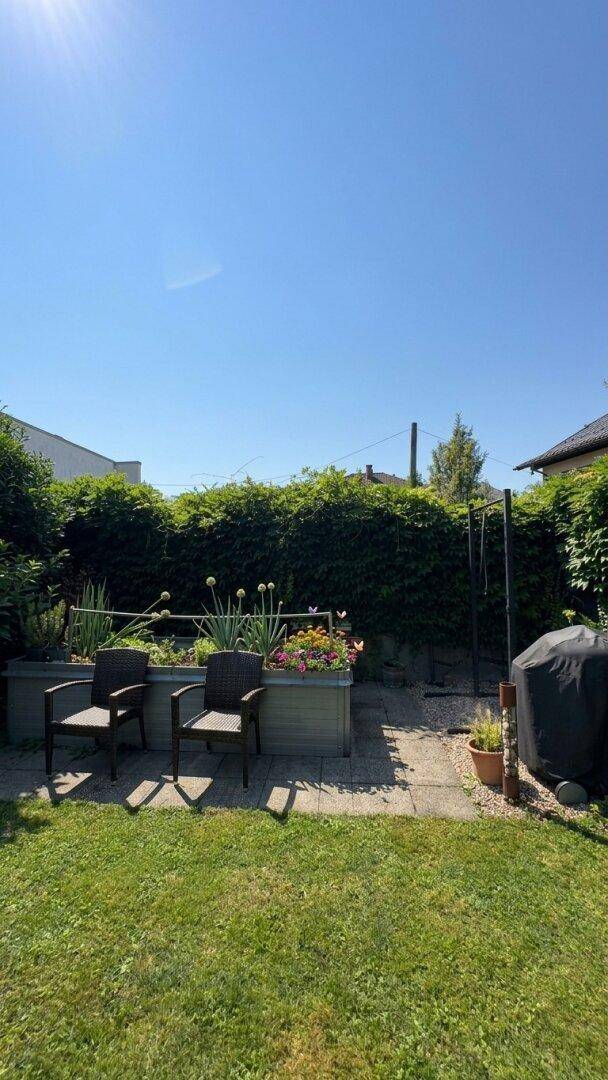 Sonniger Gartenbereich mit Rasenfläche, bepflanzten Hochbeeten und Sitzgelegenheiten im Freien.