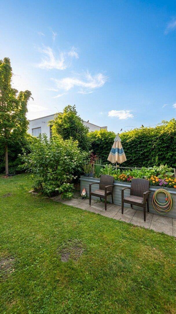 Sonniger Garten mit Rasenfläche, bunten Blumenbeeten und einer kleinen Sitzecke.