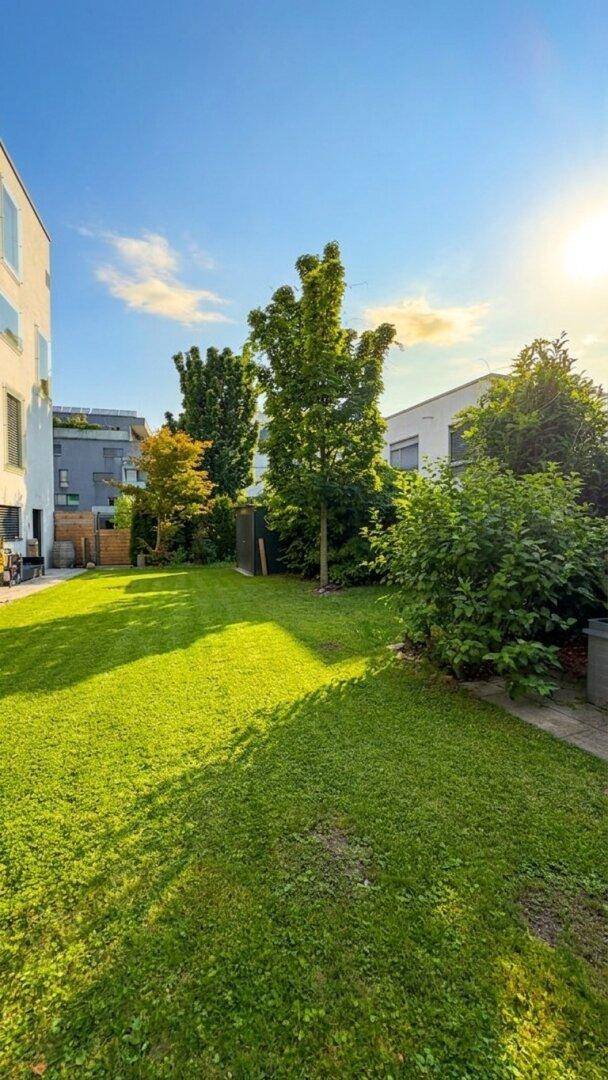 Gepflegte Rasenfläche im Gartenbereich eines modernen Wohnkomplexes unter blauem Himmel.
