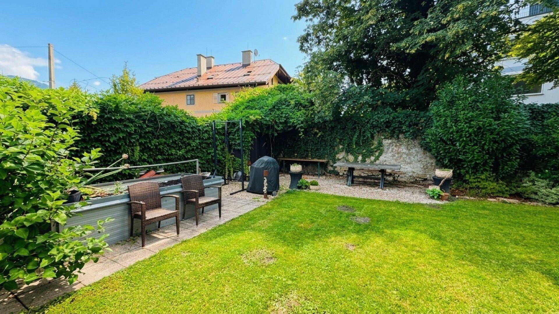 Großer Garten mit Rasen, schattenspendenden Bäumen und einem Bereich für Grillabende.