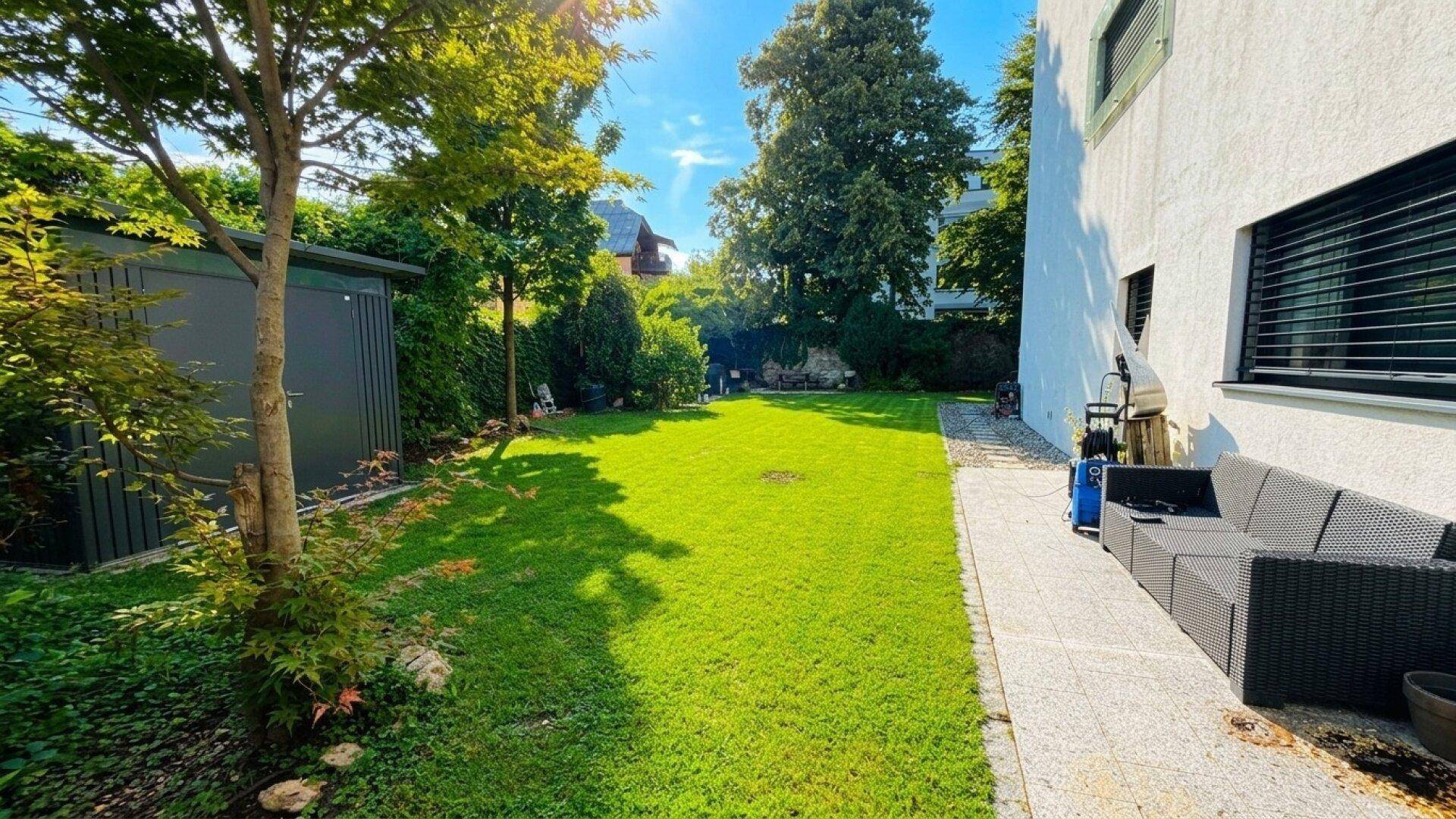 Sonniger Garten mit großer Rasenfläche, Gartenhaus und gemütlicher Sitzecke im Freien.