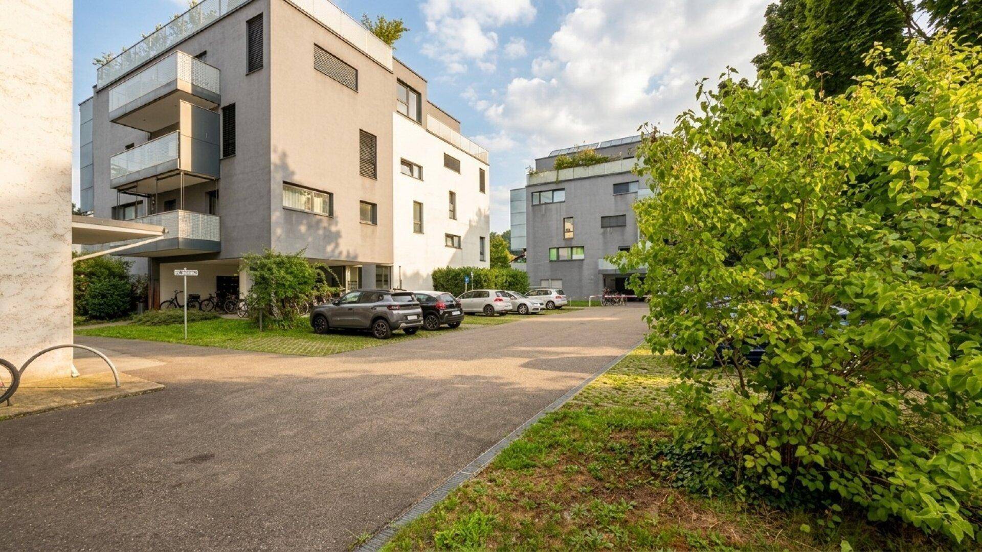 Moderne Wohngebäude mit Außenparkplätzen und gepflegten Grünflächen unter bewölktem Himmel.