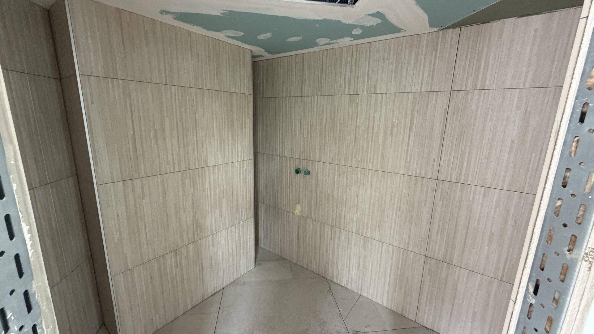 Badezimmer im Rohbau mit hellen Wandfliesen und vorbereiteter Decke für den weiteren Ausbau.