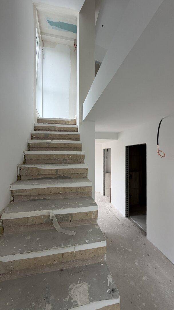 Treppenaufgang im Rohbau mit Betonstufen und weißen Wänden, bereit für den Innenausbau.