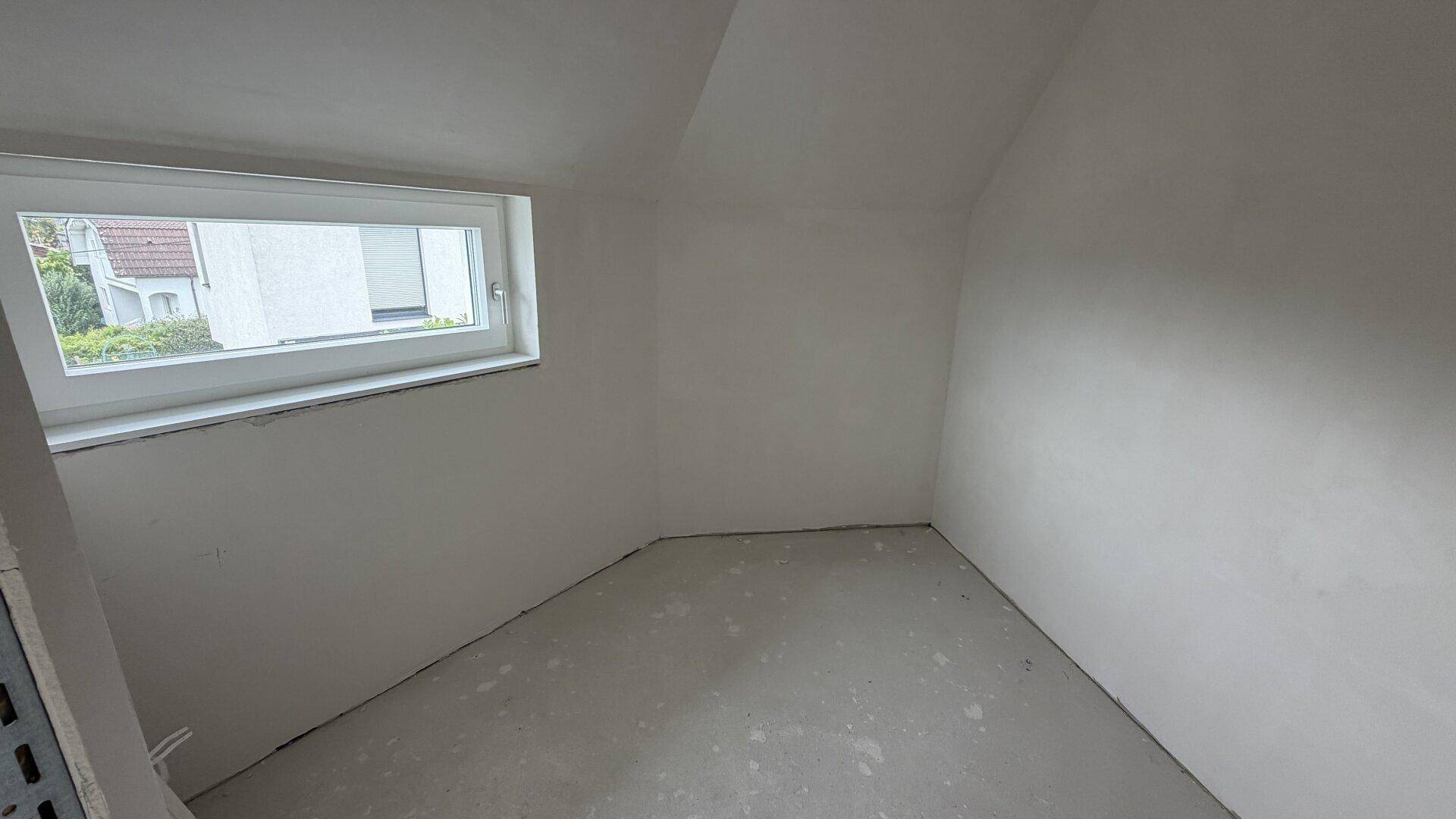 Kleines Zimmer im Rohbau mit schräger Decke und Fenster, ideal als Schlaf- oder Arbeitszimmer.