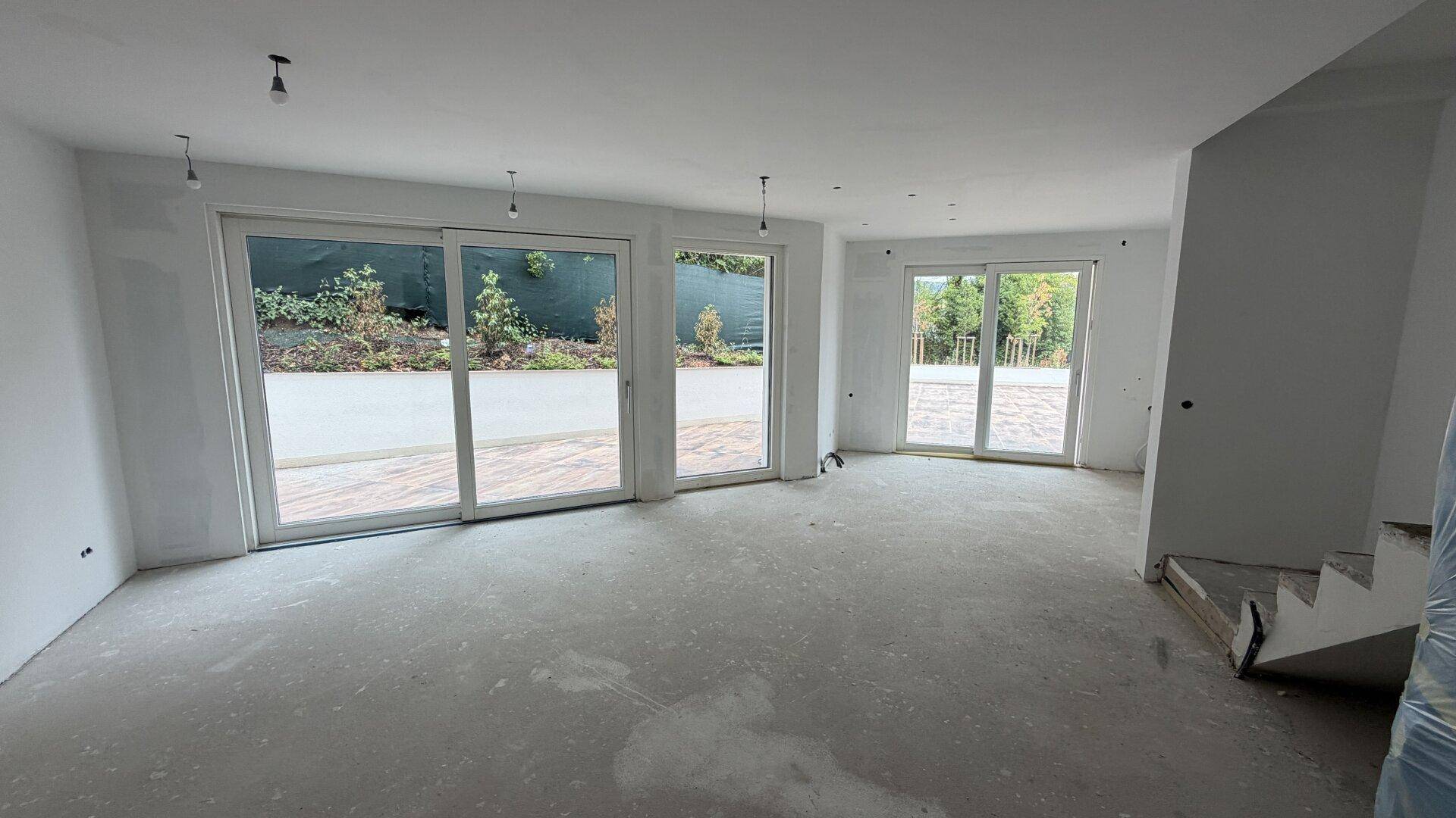 Unfertiger Wohnbereich mit großen Fensterfronten und Rohbauzustand, bereit für den Ausbau.