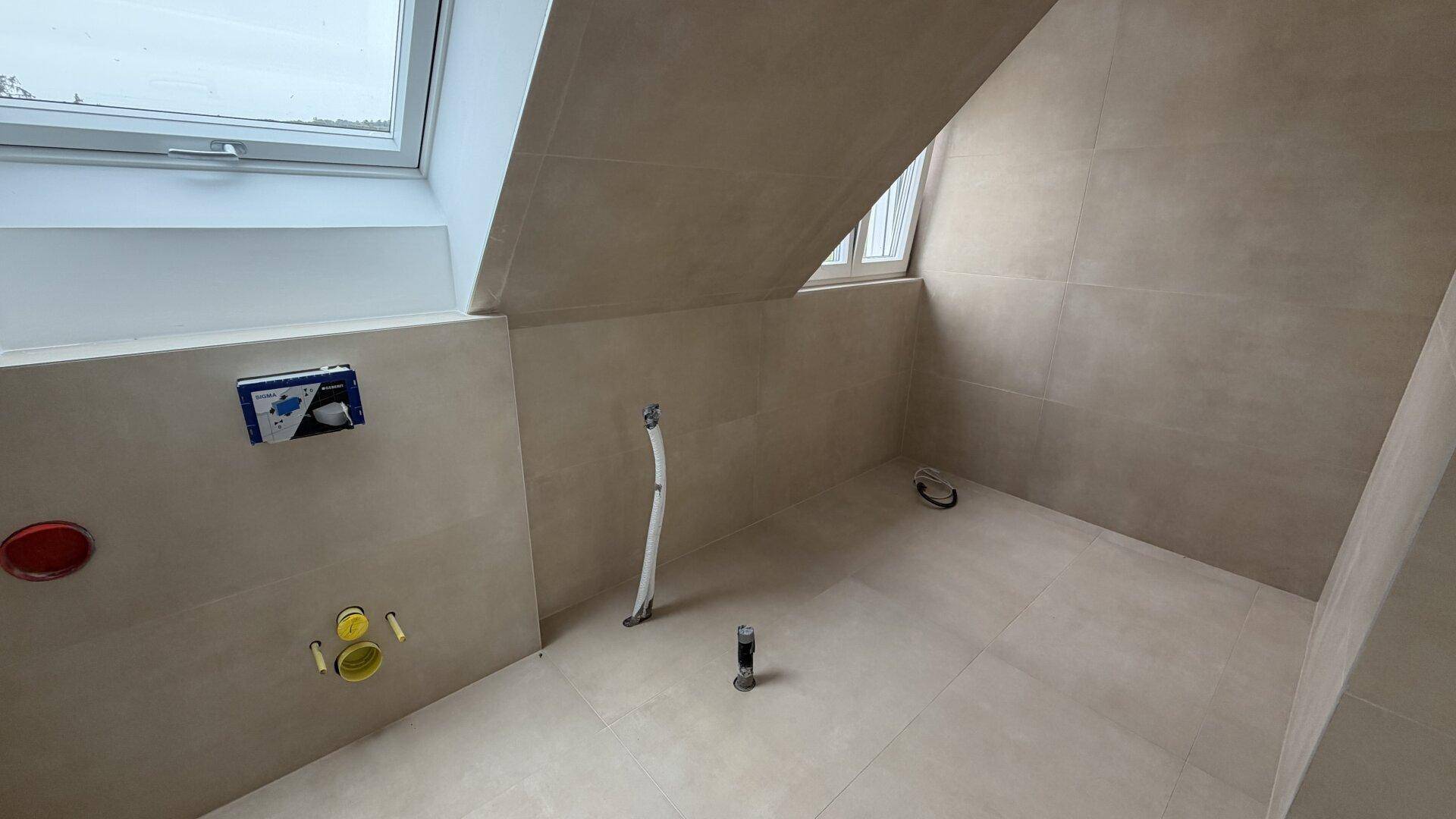 Unfertiges Badezimmer mit Installationen und Oberlicht unter der Dachschräge.