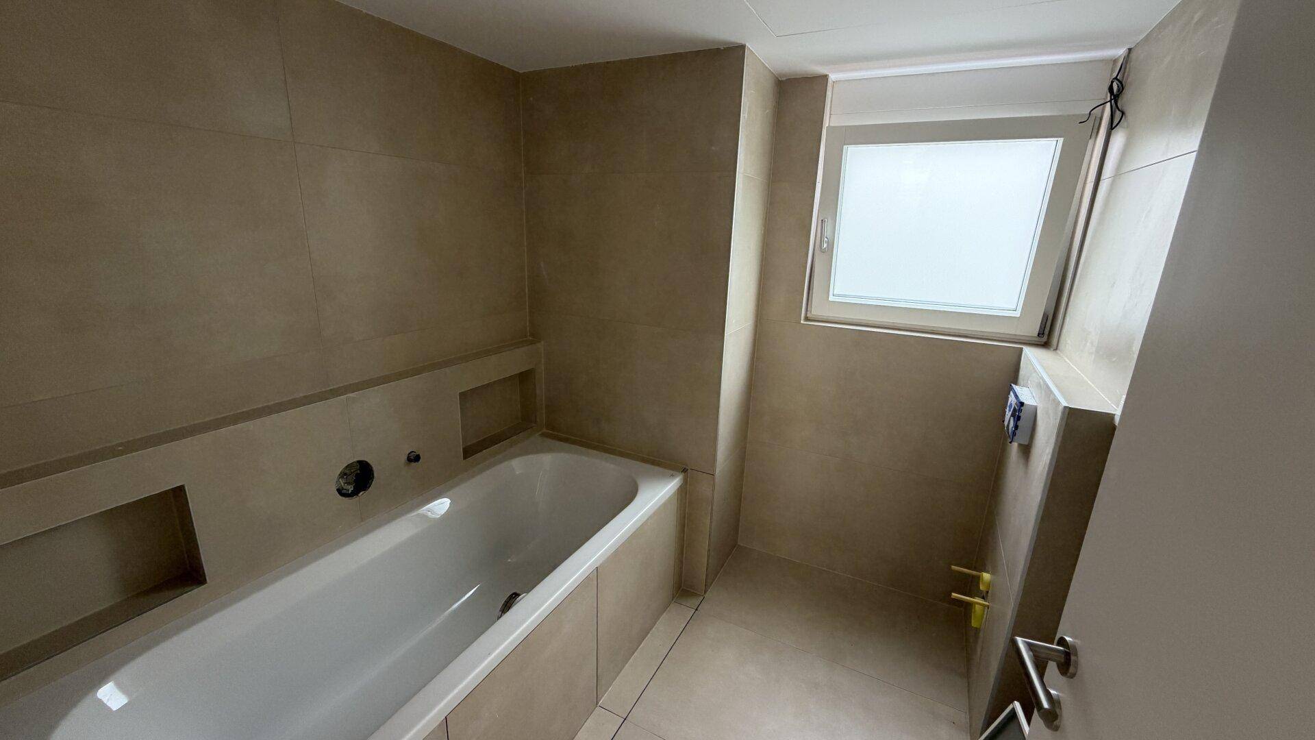 Modernes Badezimmer mit eingebauter Badewanne, beigefarbenen Fliesen und Fenster.